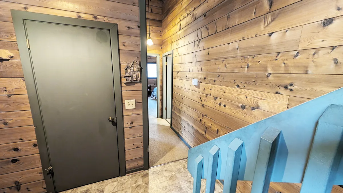 This image presents a view of wooden walls, a staircase, and a doorway, suggestive of an entry point leading outside. The perspective evokes movement through the home, with the option to step right out for trail access.
