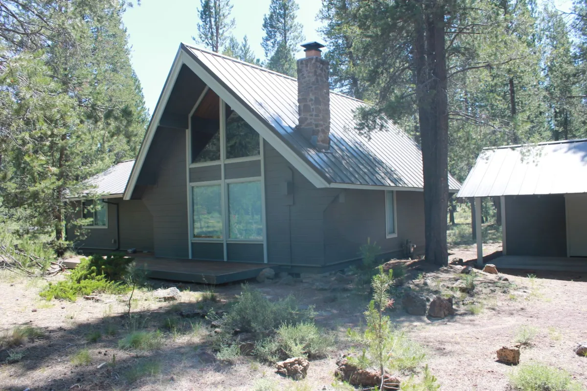 This exterior image highlights the A-frame architectural style of the home, large windows, a stone chimney, and the surrounding forest, placing the property in the context of its scenic, adventure-filled environment.