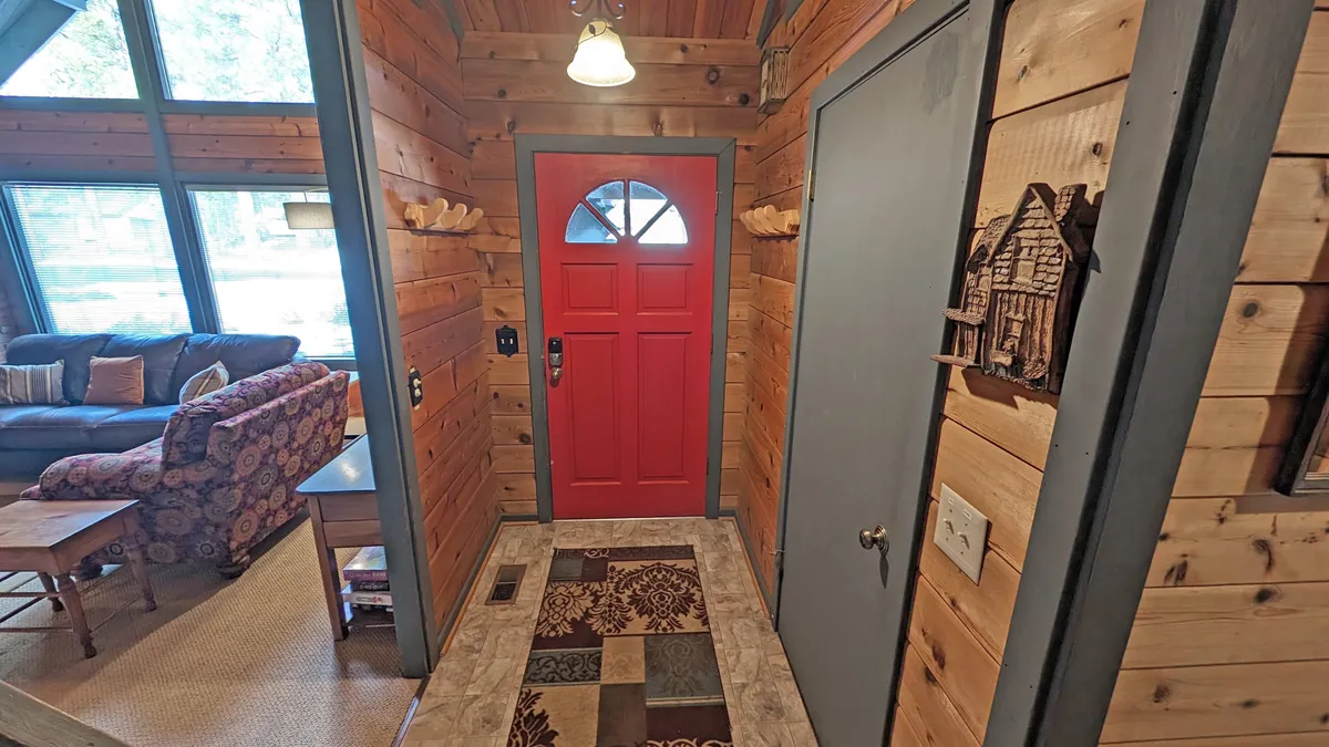This image features the red front door, rich textured wooden walls, and a cozy area rug. The scene conveys a sense of arrival and hospitality, evoking the excitement of embarking on a Sunriver adventure. The entrance area hints at transitions between indoor comfort and the outdoor activities described in the section.
