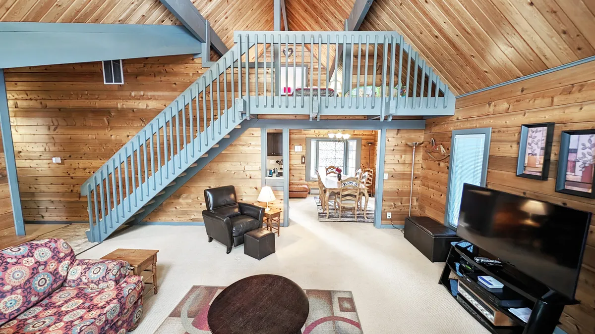 This image captures an open living layout with a visible staircase, cozy sofa, television, and dining area. The arrangement suggests areas where families can unwind after outdoor excursions, share stories of their day, and plan the next adventure together.
