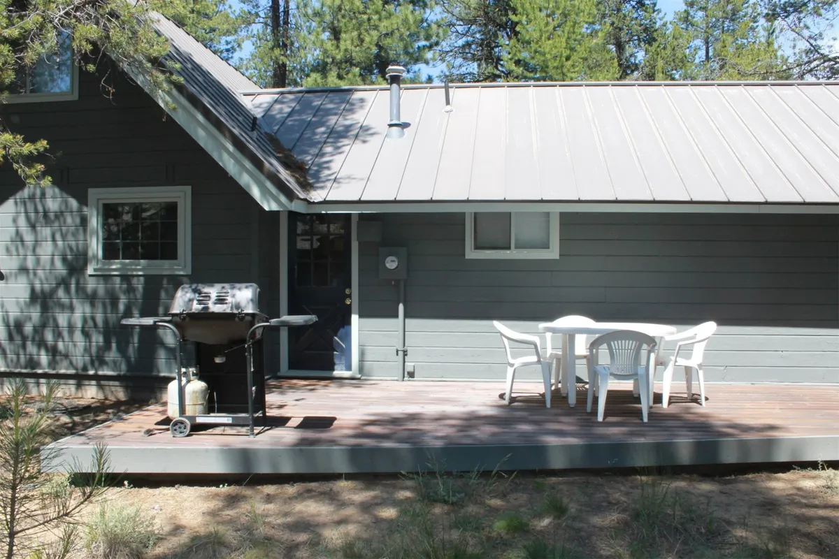 This exterior image shows a spacious wooden deck surrounded by trees, featuring a grill and a dining table set up for outdoor meals. The atmosphere is casual and inviting, perfect for gatherings and enjoying meals al fresco.