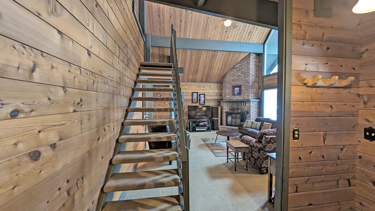 A cozy living space featuring a staircase, fireplace, and inviting seating. The wood accents and open layout suggest a seamless connection between the indoors and the natural outdoors—ideal for coming together or relaxing post-activity.